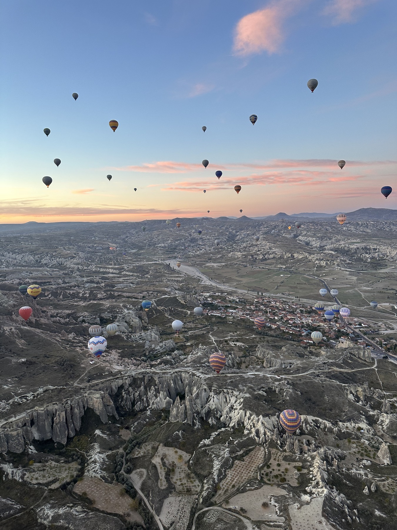 Hot air balloons rising over a valley at dawn.